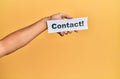 Hand of caucasian man holding paper with contact! word over isolated yellow background Royalty Free Stock Photo