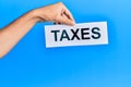 Hand of caucasian man holding paper with taxes word over isolated blue background