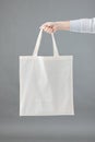 Hand of caucasian woman holding white canvas bag with copy space on grey background Royalty Free Stock Photo