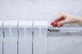 The hand of a Caucasian woman turns tap valve on a heating radiator