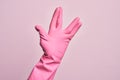 Hand of caucasian young man with cleaning glove over isolated pink background greeting doing Vulcan salute, showing hand palm and