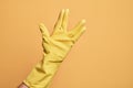 Hand of caucasian young man with cleaning glove over isolated yellow background greeting doing Vulcan salute, showing hand palm