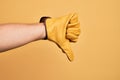 Hand of caucasian young man with gardener glove over isolated yellow background doing thumbs down rejection gesture, disapproval Royalty Free Stock Photo