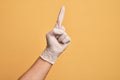 Hand of caucasian young man with medical glove over isolated yellow background counting number one using index finger, showing Royalty Free Stock Photo