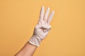 Hand of caucasian young man with medical glove over isolated yellow background counting number 3 showing three fingers Royalty Free Stock Photo