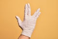 Hand of caucasian young man with medical glove over isolated yellow background greeting doing Vulcan salute, showing back of the