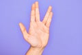 Hand of caucasian young man showing fingers over isolated purple background greeting doing Vulcan salute, showing hand palm and Royalty Free Stock Photo