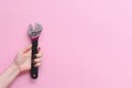 Hand of a caucasian young woman holding an adjustable monkey wrench tool on a pink background