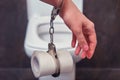 Hand chained by handcuffs to toilet paper on the background of the bowl, close-up. The concept of stomach disease, poisoning and