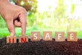 Hand changing word unsafe to safe in wooden blocks on natural background. Safety on workplace and precautionary safe acts.