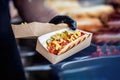 Hand of chef holding cardboard box with freshly prepared hot hot dog with tasty additions. Barbecue, grill concept Royalty Free Stock Photo