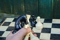 Hand with chess pieces over a chessboard against a green wall