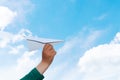 Hand of child holding a toy paper plane flying over the blue sky background. Adventure, travel and inspiration. Message concept