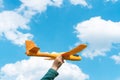 Hand of child holding a toy plane flying over the cloudy blue sky background. Adventure, travel and vacation concept Royalty Free Stock Photo