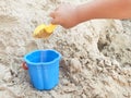 Hand of child playing in the sandbox with yellow scoop and blue bucket