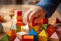 the hand of a child trying to build a tower of colored wooden cubes