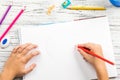 Hand of children drawing red heart with colored pencil on white paper on wooden table