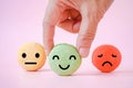 Hand choose happy face icon on green macaron with blurred others on sweet pink background