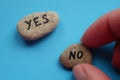 The hand chooses a stone with the text No. Stone with the word Yes on a blue table. Choice concept Royalty Free Stock Photo