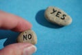 The hand chooses a stone with the text No. Stone with the word Yes in blur on a blue table. Choice concept Royalty Free Stock Photo