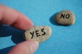 The hand chooses a stone with the text Yes. Stone with the word No in blur on a blue table. Choice concept Royalty Free Stock Photo