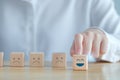 Hand choosing happy face among unhappy faces on wooden blocks. Positive thinking, Mental health assessment. Royalty Free Stock Photo