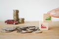 Hand choosing increasing graph sign on wooden cube block on pile of coins with blurred stack of coins and red miniature car Royalty Free Stock Photo