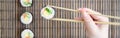 A hand with chopsticks holds a sushi roll on a bamboo straw serwing mat background. Traditional Asian food Royalty Free Stock Photo