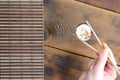 A hand with chopsticks holds a sushi roll on a bamboo straw serwing mat background. Traditional Asian food Royalty Free Stock Photo