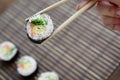 A hand with chopsticks holds a sushi roll on a bamboo straw serwing mat background. Traditional Asian food