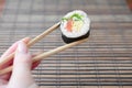 A hand with chopsticks holds a sushi roll on a bamboo straw serwing mat background. Traditional Asian food Royalty Free Stock Photo