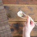 A hand with chopsticks holds a sushi roll on a bamboo straw serwing mat background. Traditional Asian food Royalty Free Stock Photo