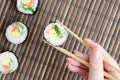 A hand with chopsticks holds a sushi roll on a bamboo straw serwing mat background. Traditional Asian food Royalty Free Stock Photo