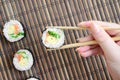 A hand with chopsticks holds a sushi roll on a bamboo straw serwing mat background. Traditional Asian food Royalty Free Stock Photo