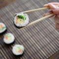 A hand with chopsticks holds a sushi roll on a bamboo straw serwing mat background. Traditional Asian food Royalty Free Stock Photo