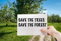 Hand with a clean white sheet with the inscription save the trees save the forest on a background of green forest landscape, the c