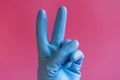 Hand with cleaning glove making peace. Hand in a rubber glove on a pink background