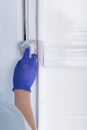 The hand of a cleaning service worker in a protective glove wipes the refrigerator with a sponge with cleaning foam Royalty Free Stock Photo