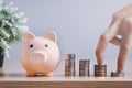 The hand is climbing up the coin stack with a pig piggy bank on a wooden floor In the morning, at home, the concept of saving Royalty Free Stock Photo