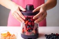 hand closing a blender lid with mixed berries for a smoothie