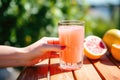 hand clutching a cold glass of grapefruit juice on a hot day