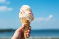 Hand clutching an ice cream cone against a bright blue sky