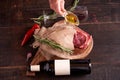 Hand, with a container of olive oil, next to a piece of juicy, seasoned rib eye steak wrapped in paper and burlap