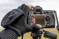 A hand covered in a woolen glove with only the fingertips uncovered adjusts a camera on a tripod in the winter season Royalty Free Stock Photo