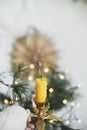 Hand in cozy sweater holding vintage candlestick with burning candle on background of warm lights, fir branches, sweden star in