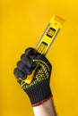 Hand of a craftsman in a glove holds a building level on a yellow background. Idea for building or renovation Royalty Free Stock Photo