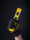 A hand of craftsman in glove holds a construction level of yellow color on a dark background. Idea for building or renovation Royalty Free Stock Photo