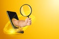 The hand crawling out through the smartphone holds, offers a magnifying glass on a yellow background. Online search concept,