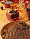 Hand cupping dark roasted coffee beans with wooden spoon into coffee grinder for preparing homemade coffee