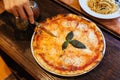 Hand cut a slice of Margarita pizza topping with basil leaves served with oregano and chili powder Royalty Free Stock Photo